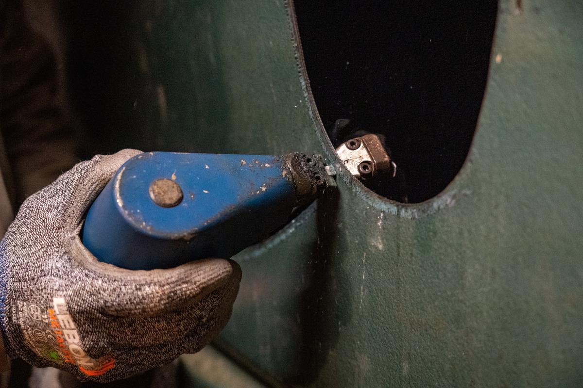 Gros plan sur la découpe d’une paroi de cuve à fioul avec un outil de coupe manuel
